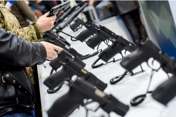 A table display of new guns with customers browsing