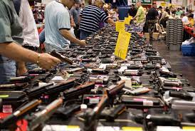 Gun show table with firearms on display and customers browsing