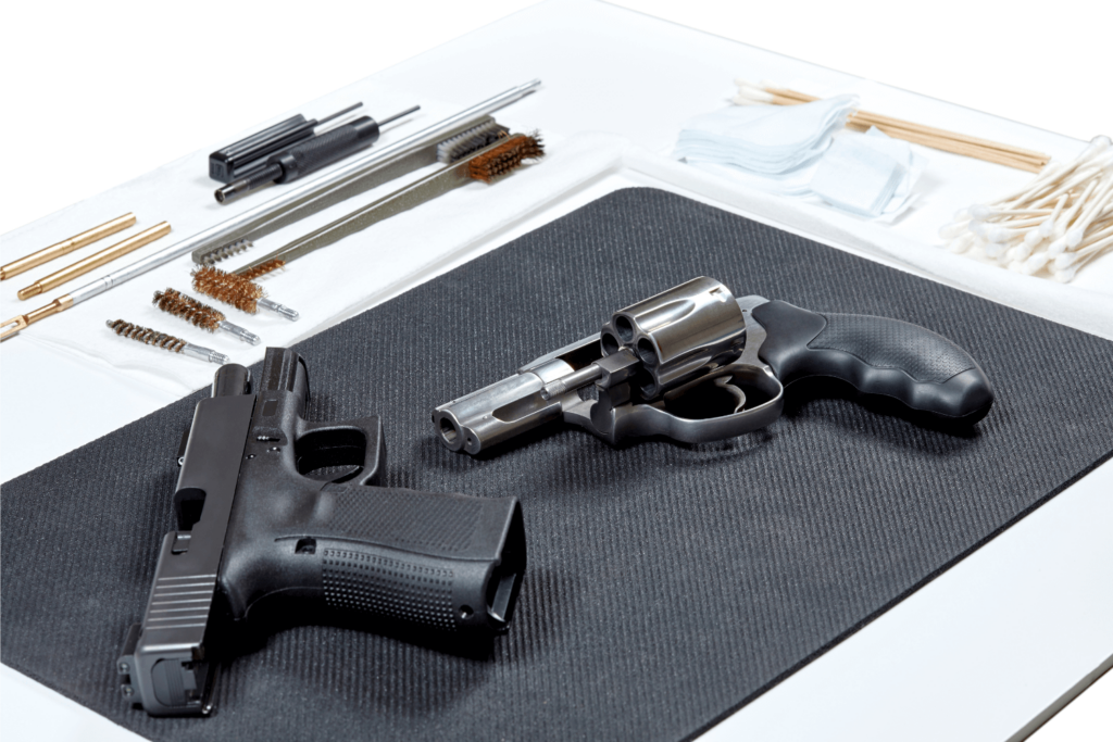 Two firearms and firearm cleaning supplies placed on a black mat