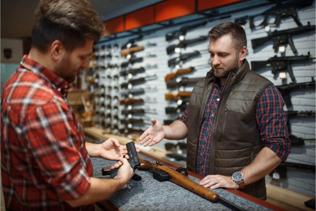 Man inspecting a firearm while a gun shop owner speaks to him
