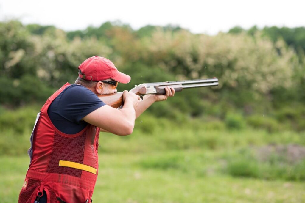 Man wearing a red vest shooting a shotgun at a shooting range