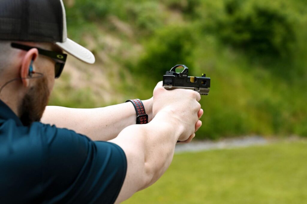 Man at an Outdoor Gun Range Wearing Protective Eyewear and Earwear While Aiming His Custom Pistol at a Target