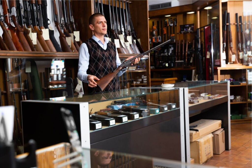 Man Standing Behind the Counter Holding a Gun Inside of a Standard Gun Shop