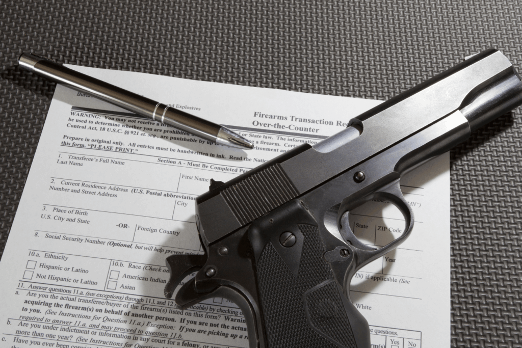 a Black Firearm a Legal Document and a Black Pen Displayed on a Black Background