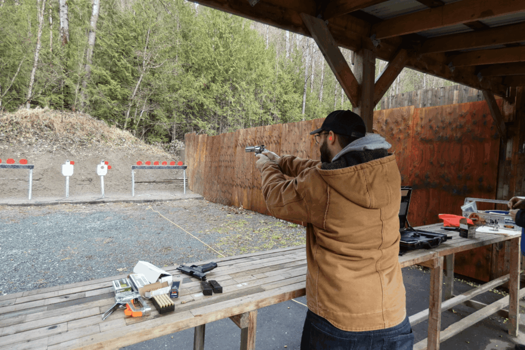 An outdoor shooting range with a man in a tan coat aiming his firearm at a target - Pennsylvania Gun Shows | Get Tickets For Eagle Shows an Outdoor Shooting Range with a Man in a Tan Coat Aiming His Firearm at a Target