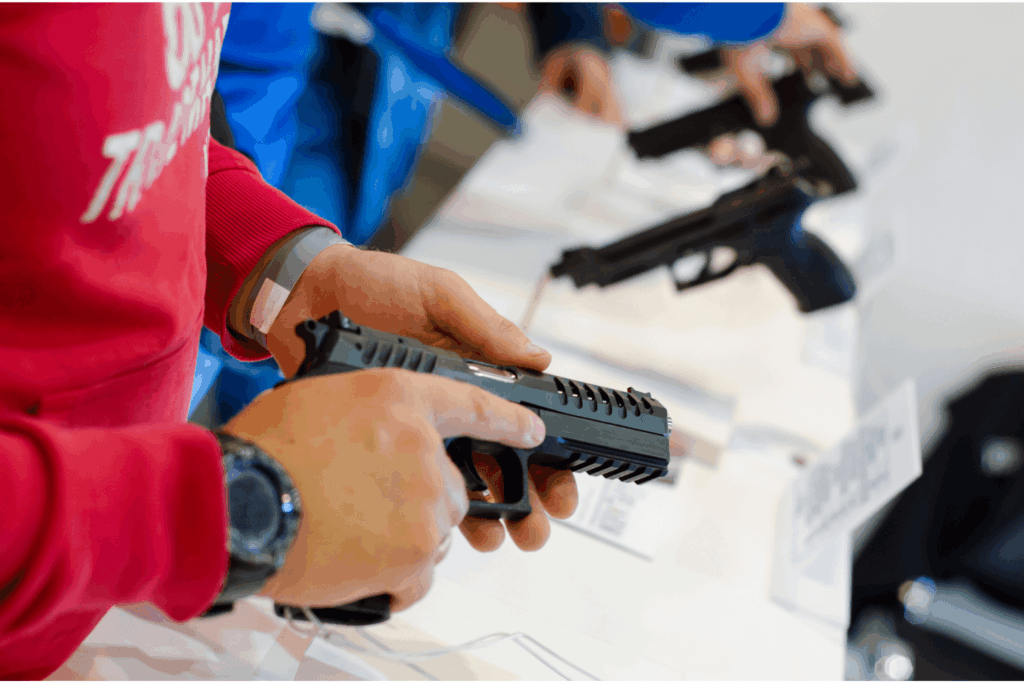 Man Holding a Pistol While Browsing at a Gun Show Vendor Table